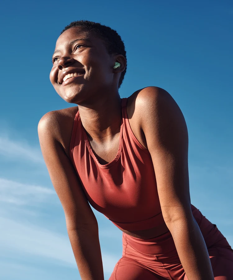 Happy woman in coral athletic wear smiling during outdoor fitness workout break against blue sky